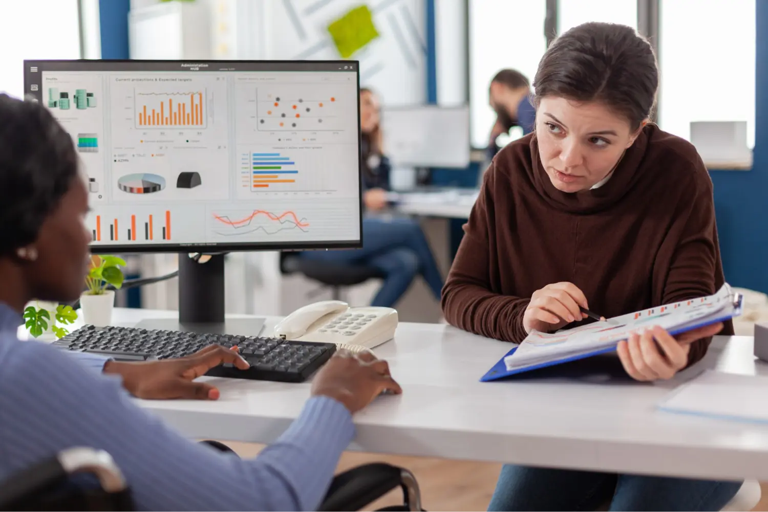 Colleagues review analytics charts on a monitor and in a folder