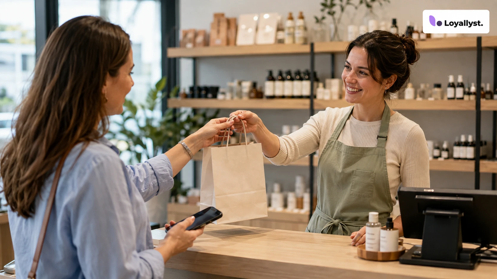 A customer holding a smartphone receives a purchase from a shop assistant in a cosmetics store, with the Loyallyst logo