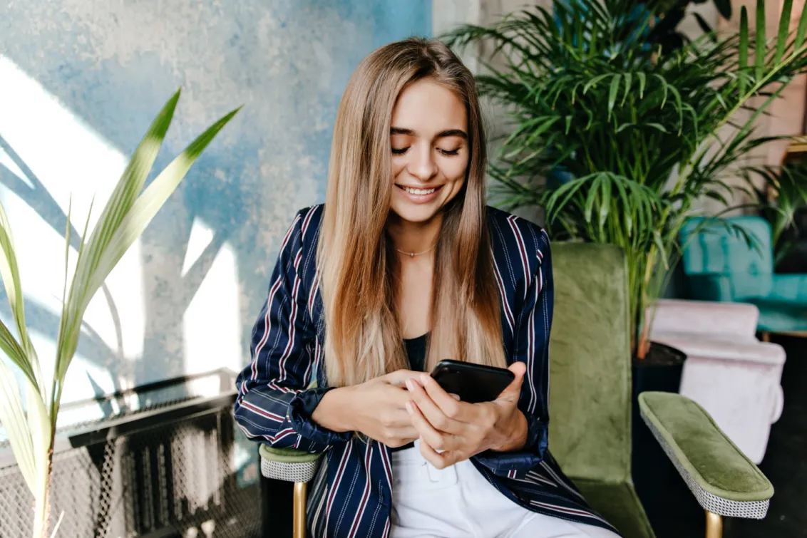 A woman uses a smartphone while sitting in an armchair among indoor plants