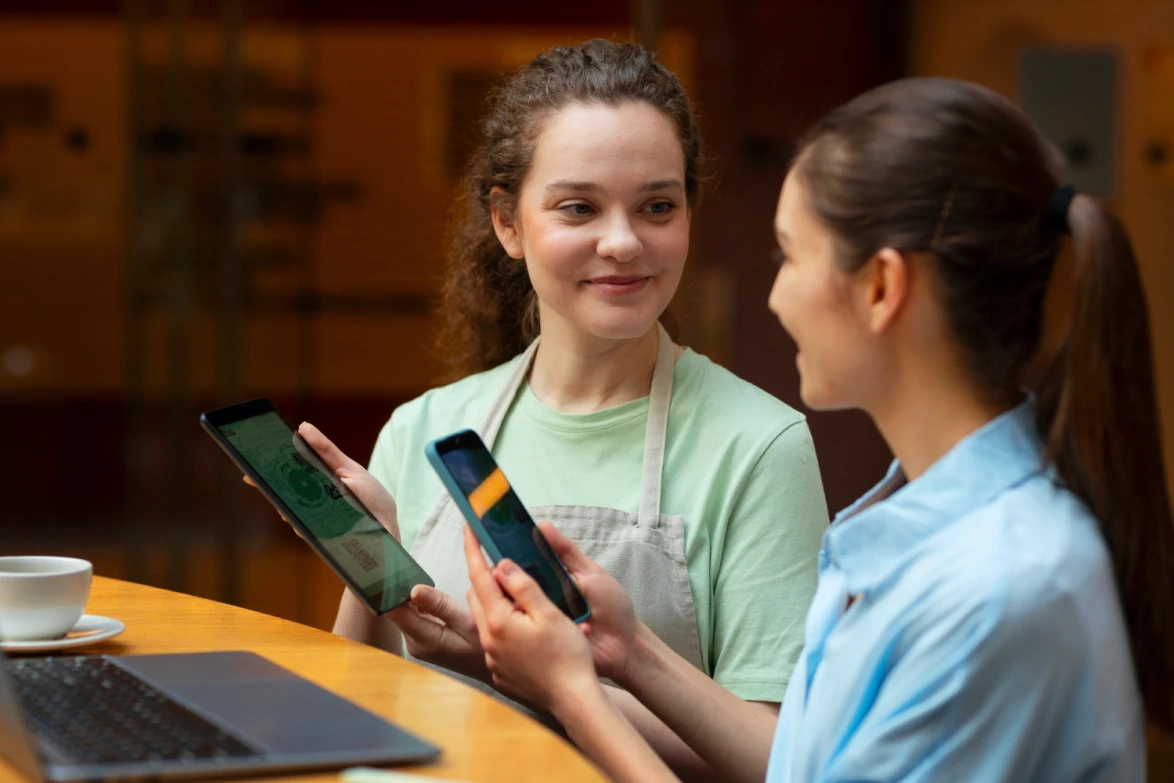A café employee with a tablet talks to a customer holding a smartphone